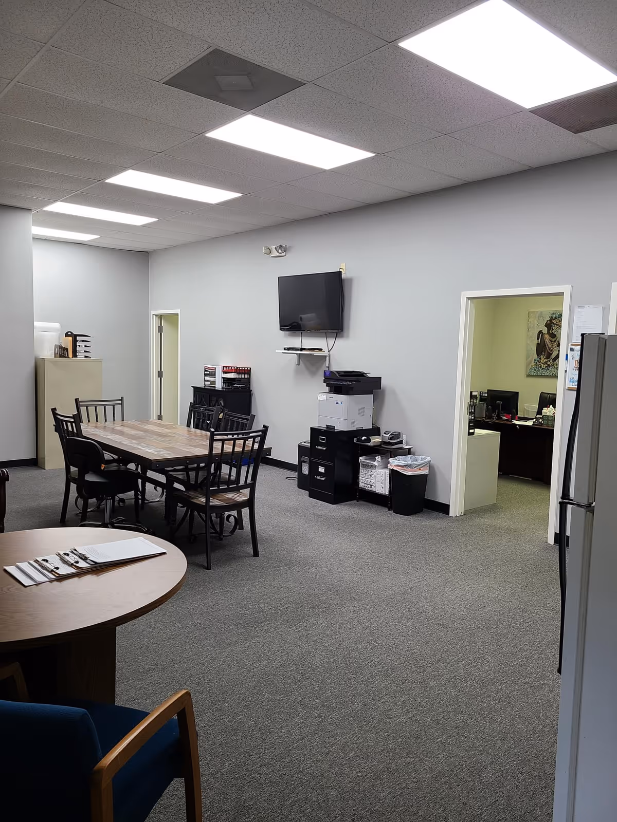 Interior common area with tables, chairs, a wall-mounted TV, and office equipment.