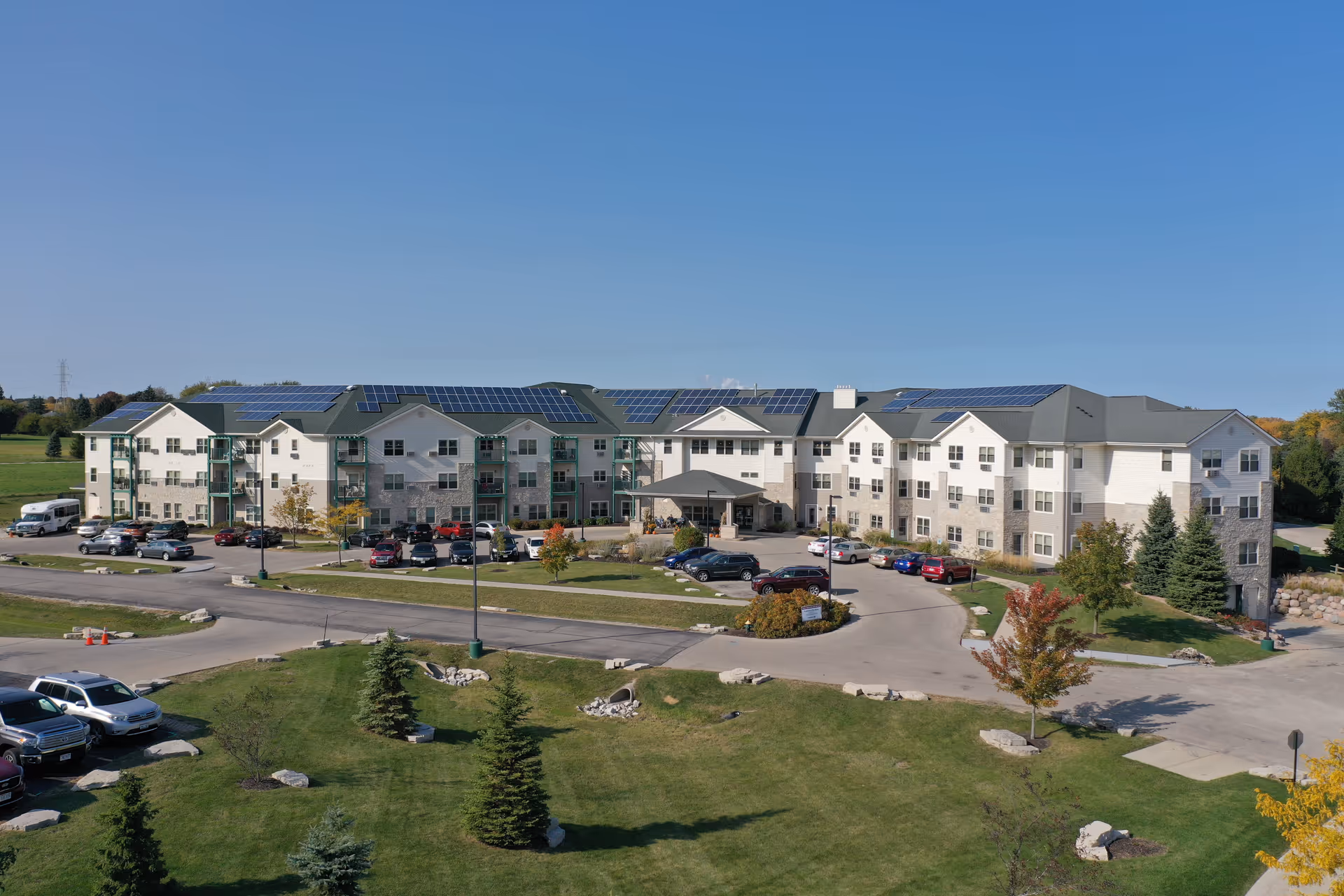 A large multi-wing senior living facility with solar panels, parked cars, and green landscaping.