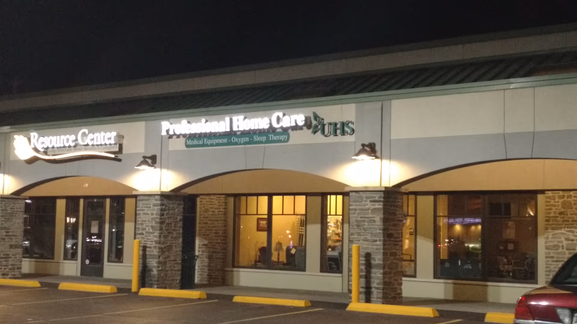 Night exterior of a storefront strip with stone columns and lit signs.