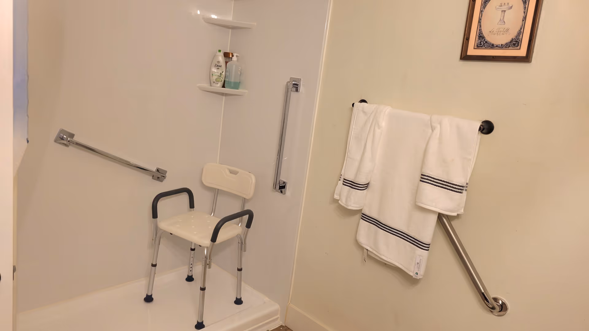 Accessible bathroom with shower chair, grab bars, and towels in a residential facility.