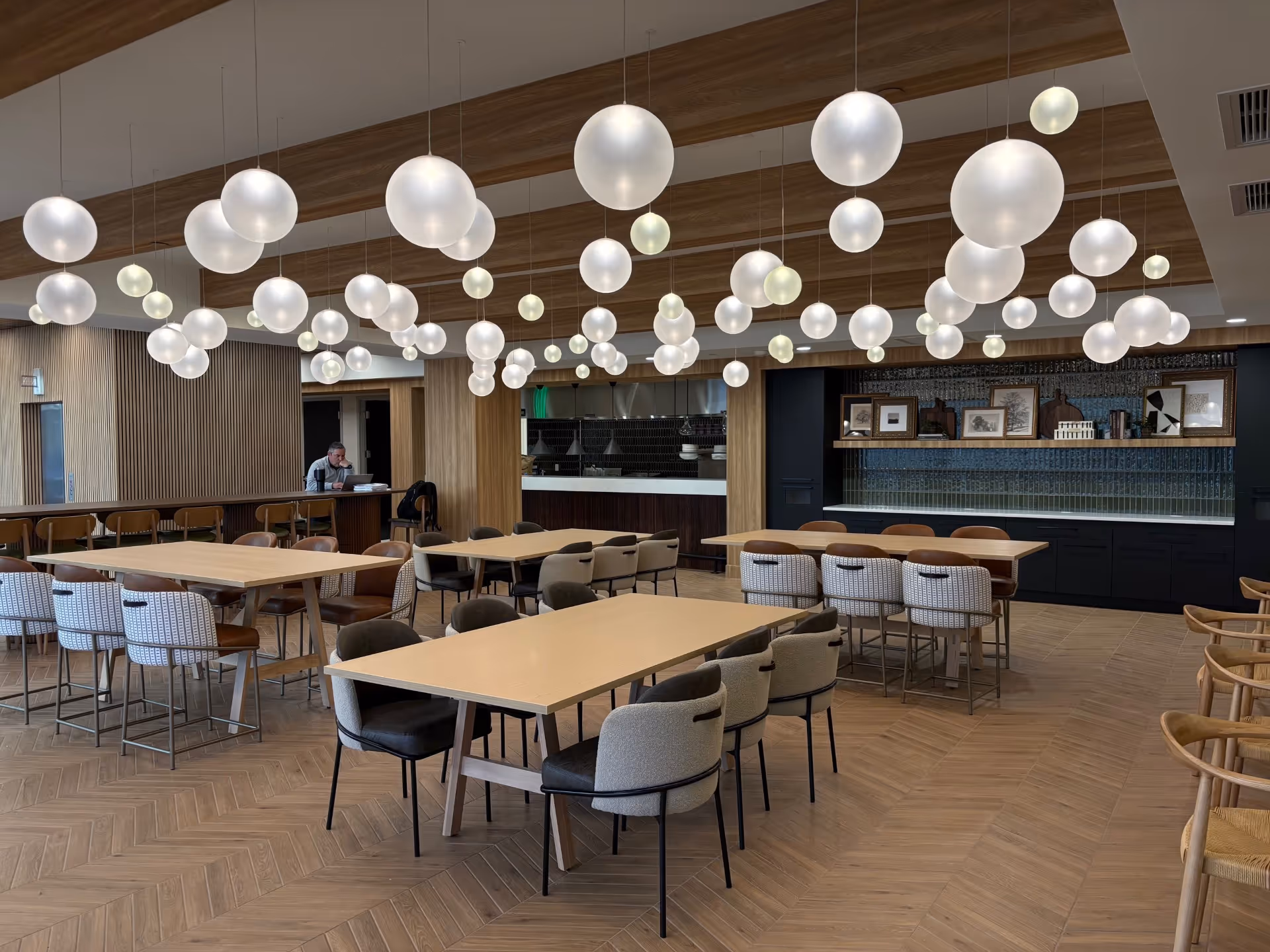 A modern dining hall with multiple tables, chairs, and a bar area.