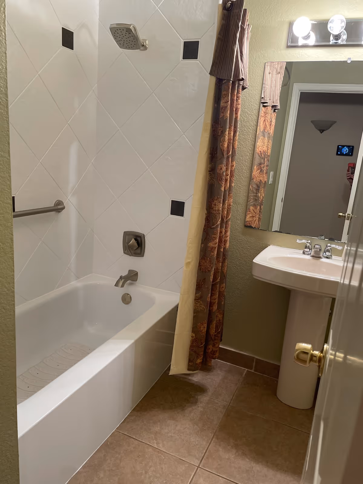 Bathroom with a bathtub, shower curtain, pedestal sink, mirror, and tiled walls.