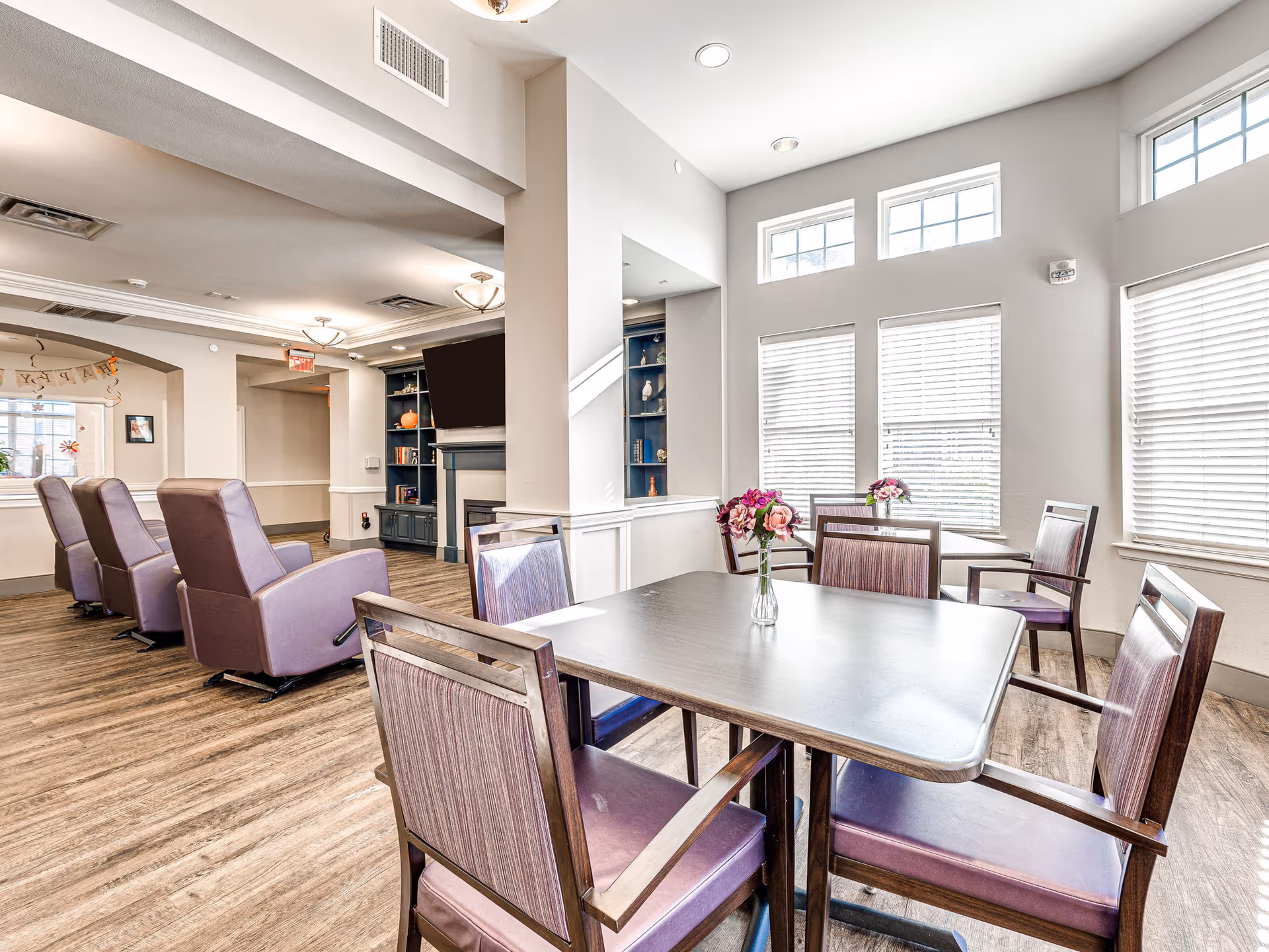 Bright communal lounge with purple chairs around a metal table and large windows.