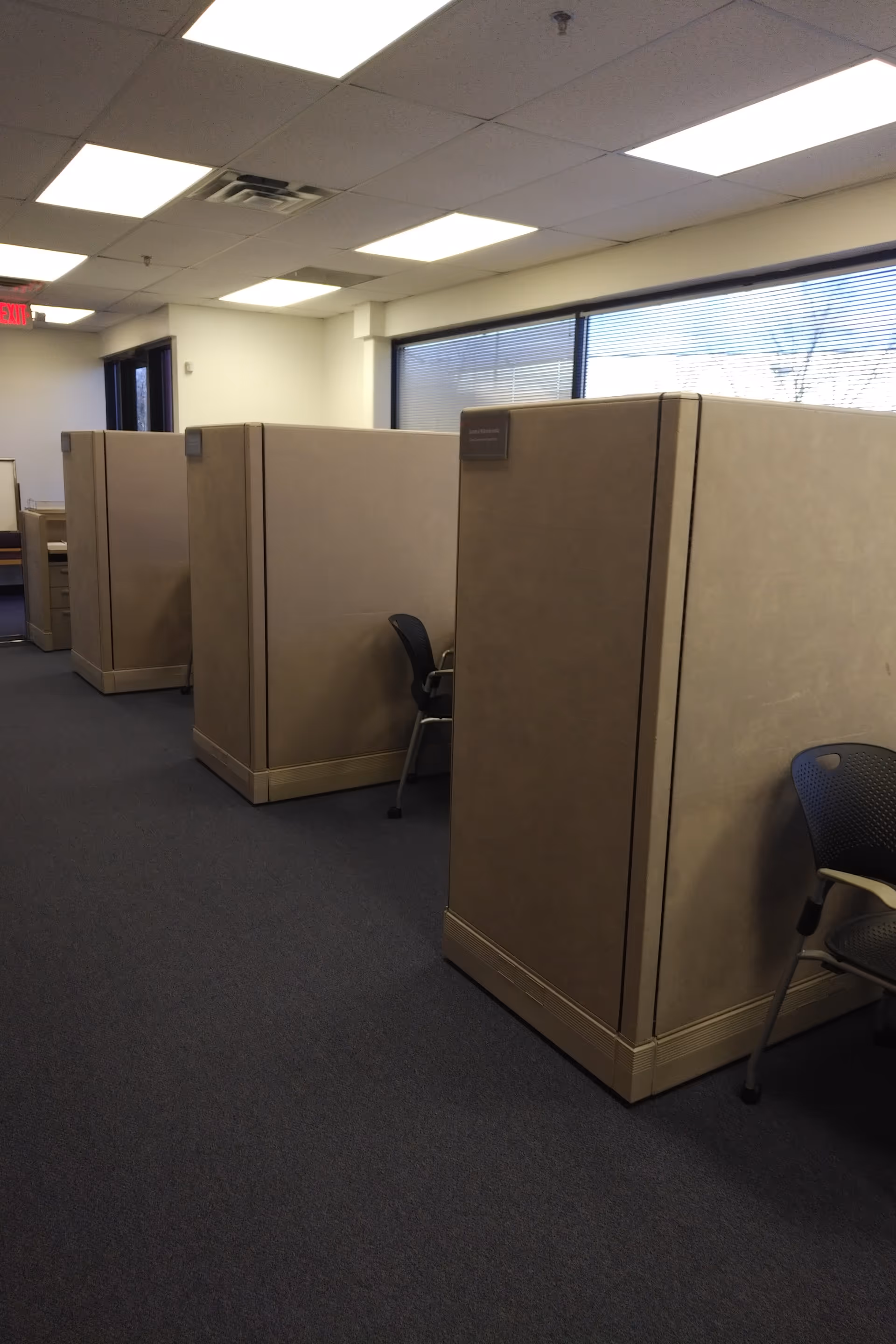 Row of beige office cubicles fills a carpeted, fluorescent-lit interior.