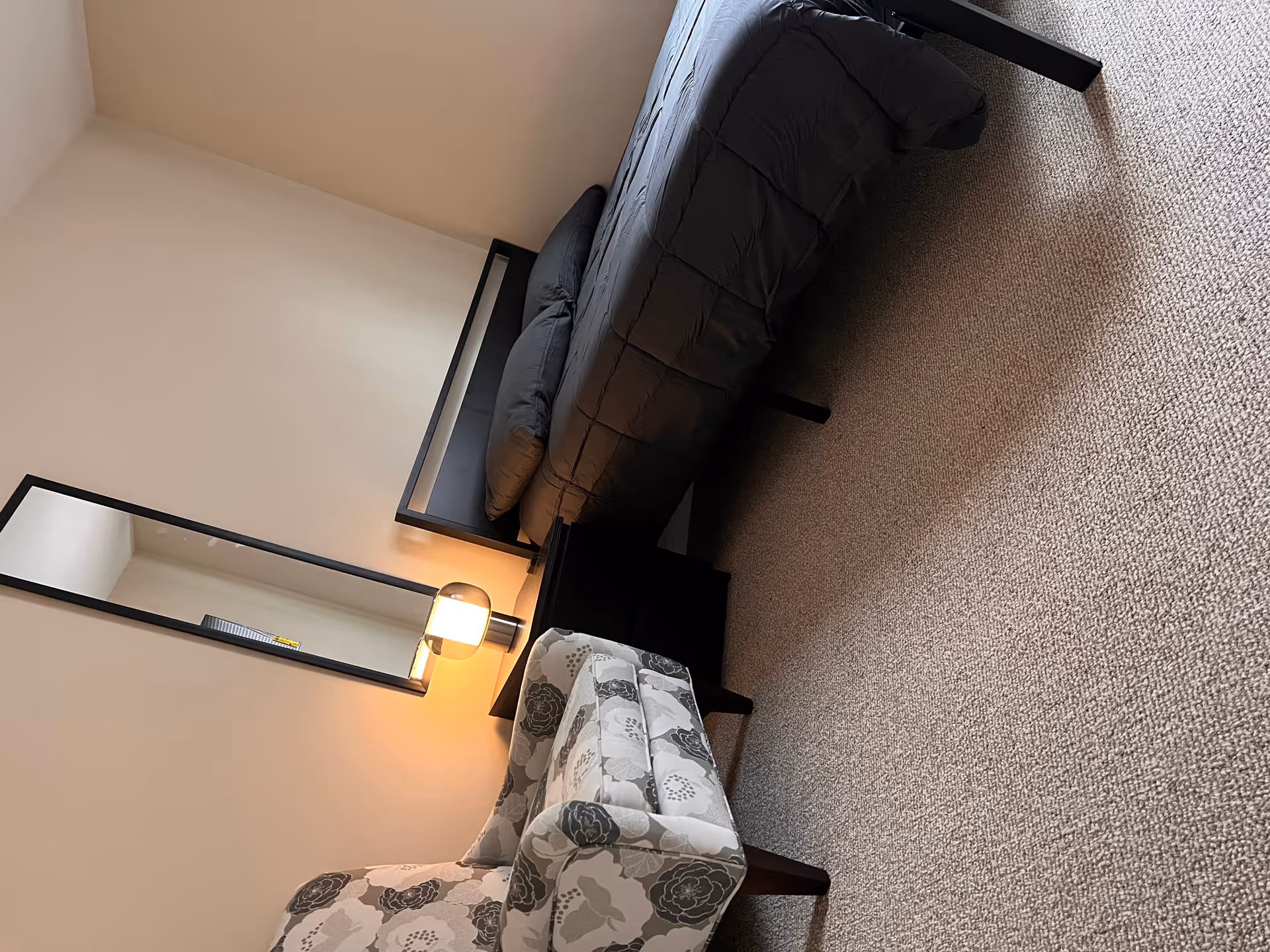Senior living facility bedroom with bed, chair, nightstand, and wall mirror.