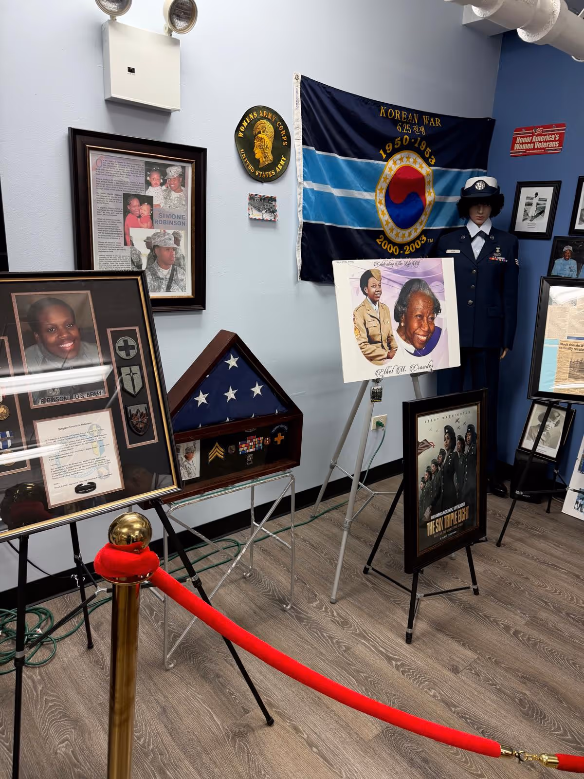 Indoor memorial display with framed photos, flag, and military memorabilia.