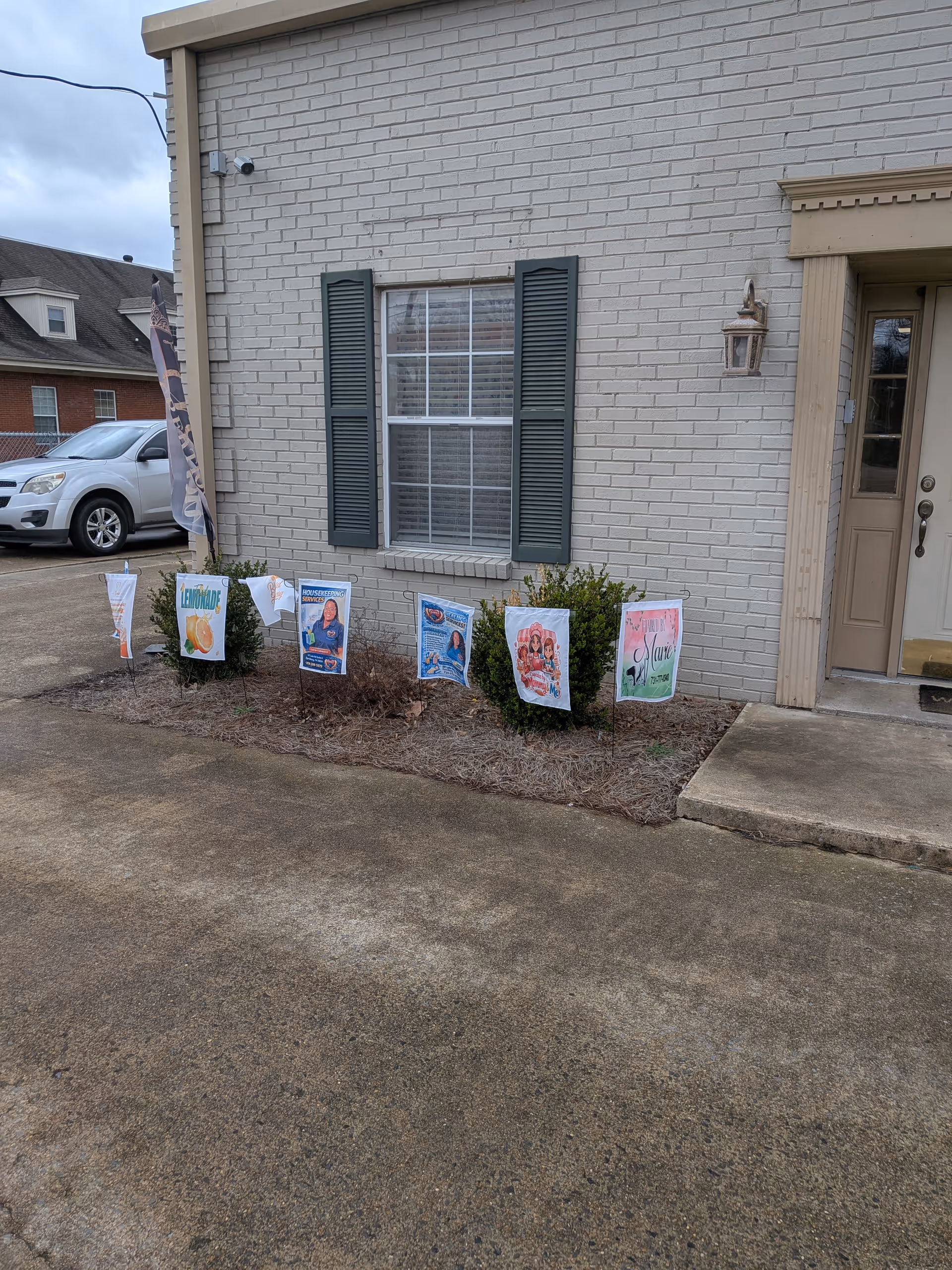 Front exterior of a beige brick building with a window, door, and banner signs.