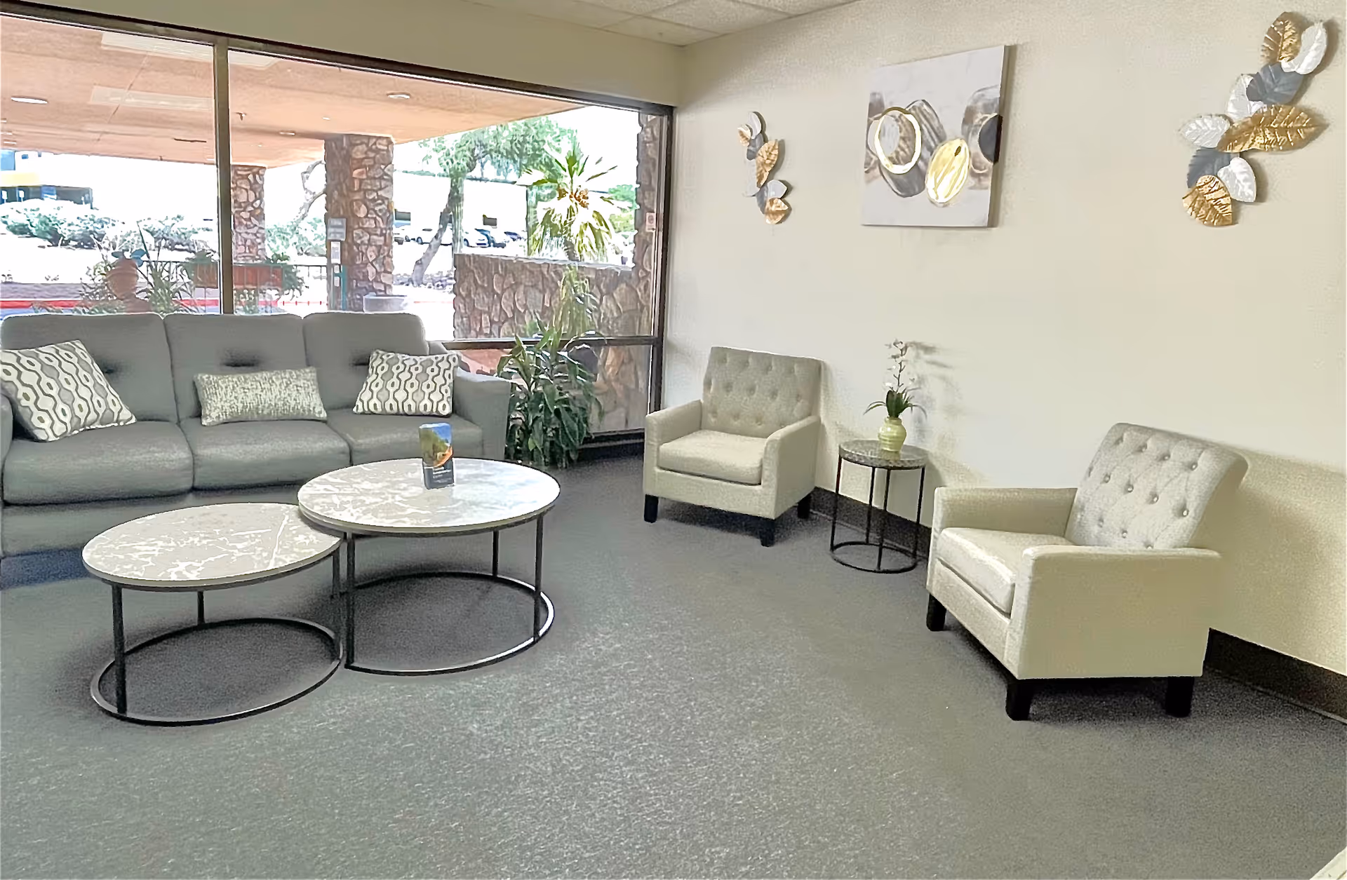 Bright lounge area with a sectional sofa, two armchairs, and round coffee tables by a window.