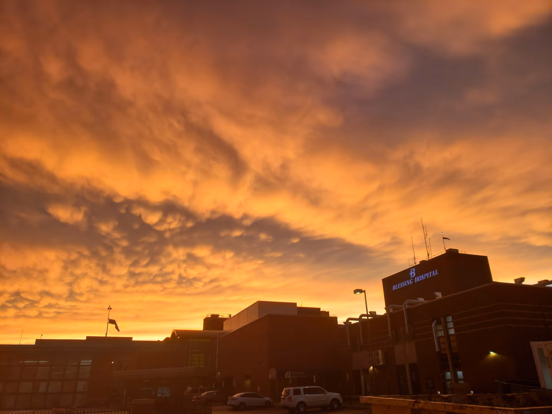 Exterior of Blessing Hospital at sunset with fiery orange sky.