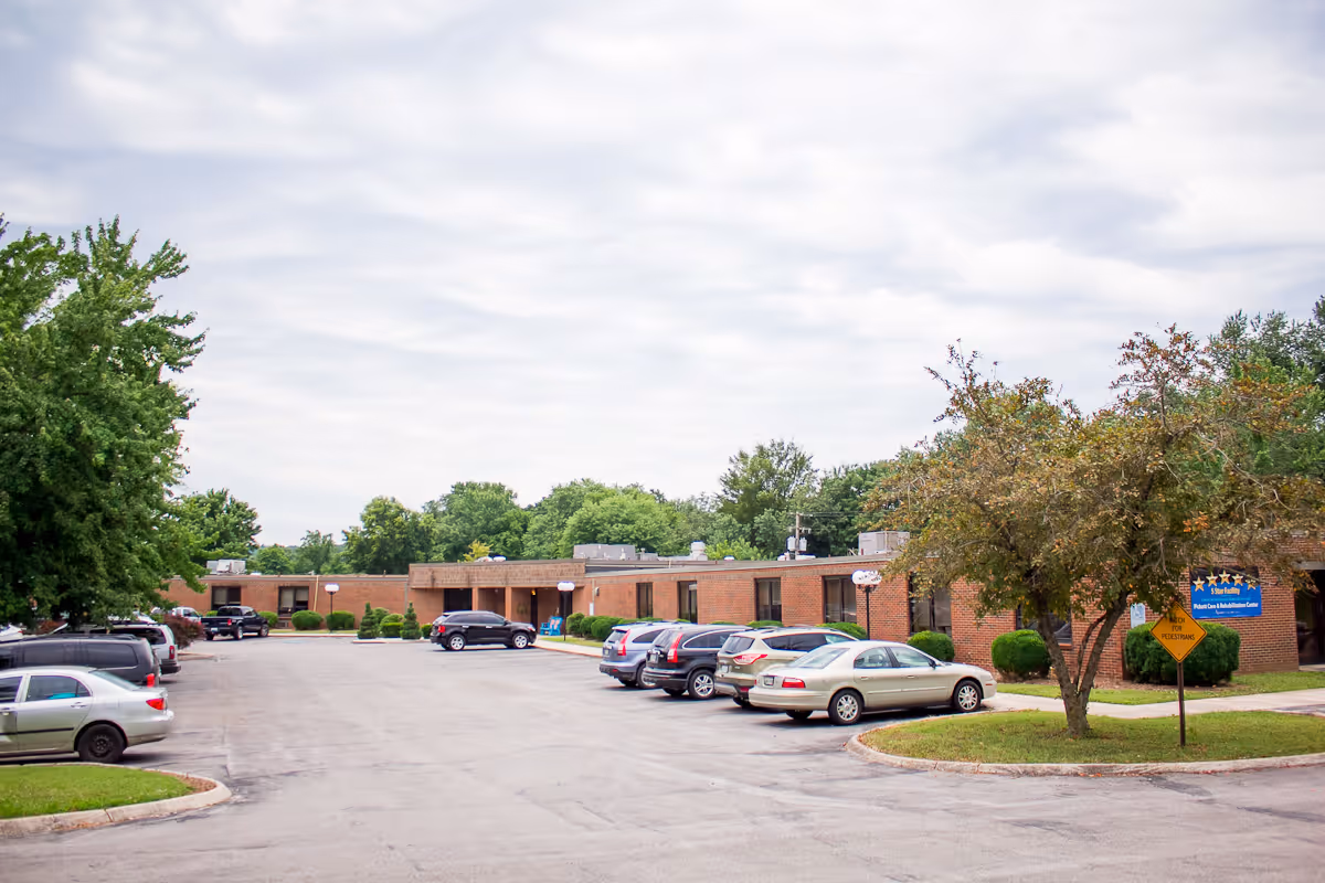 Exterior view of Pickett Care and Rehabilitation Center showing a single-story brick building with several parked cars in front. Trees and greenery surround the parking lot under a cloudy sky.