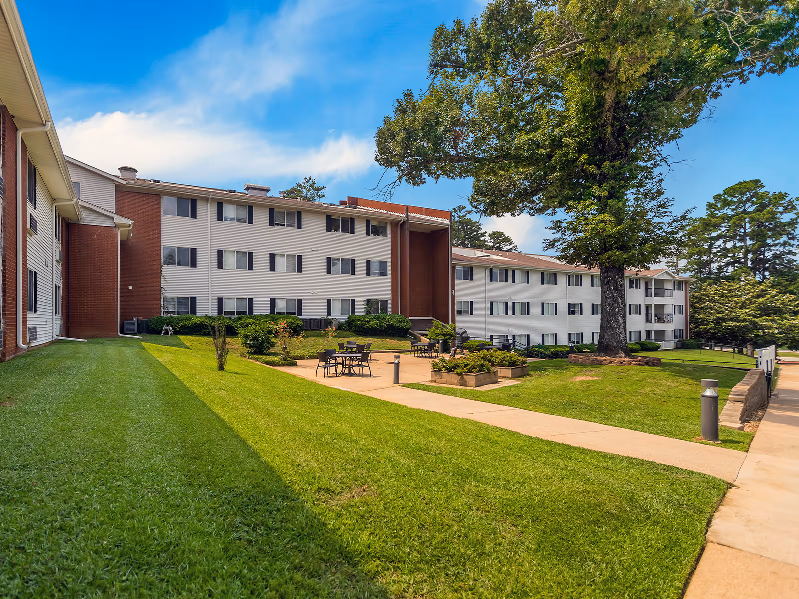Exterior view of a multi-story senior living building with a lawn, trees, and a patio.