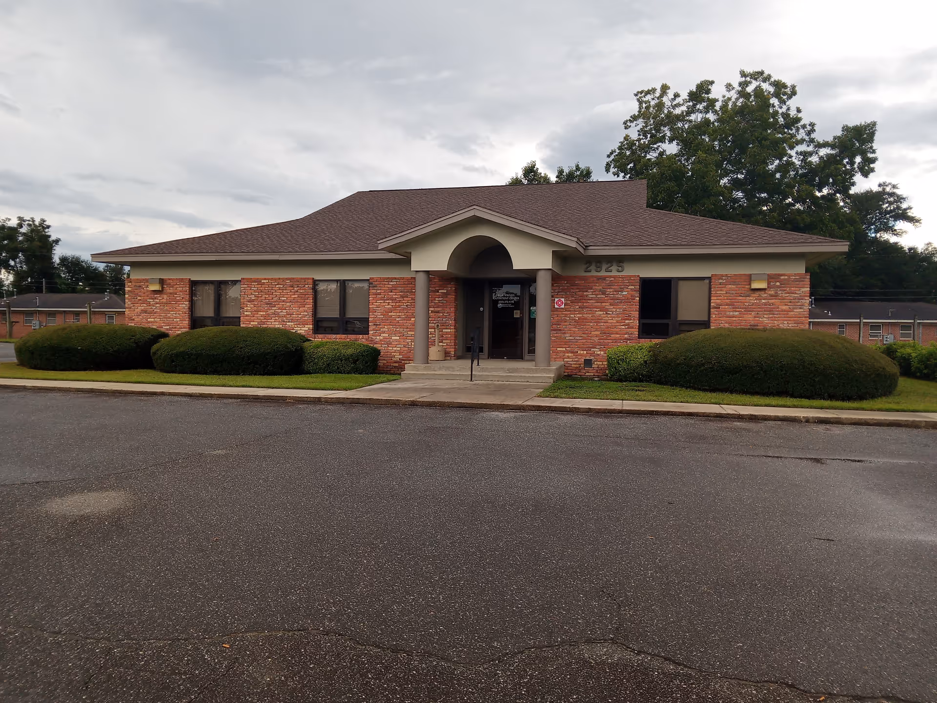 Brick outpatient center with a central arched entrance, brick facade, and trimmed bushes.