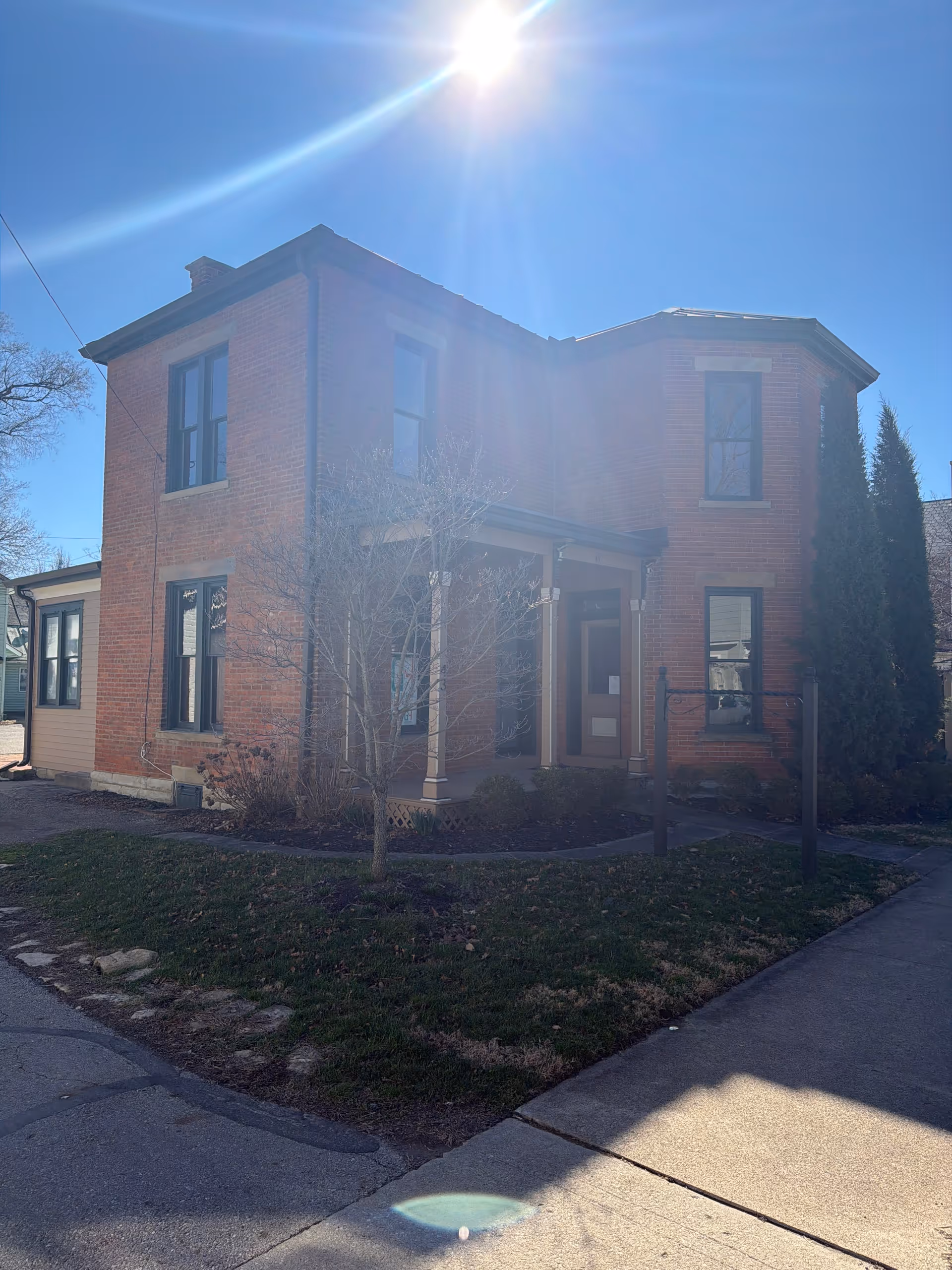 Brick two-story building with a front porch and bright sun overhead.