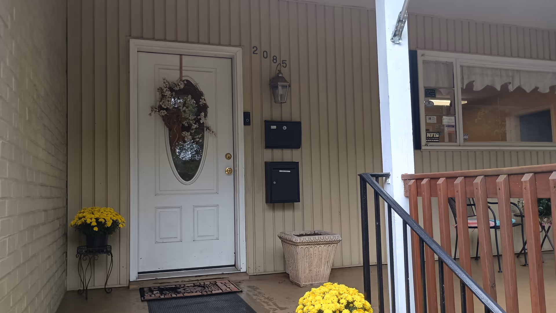 Front entrance of Karis Care Services, white door with wreath and yellow potted chrysanthemums.