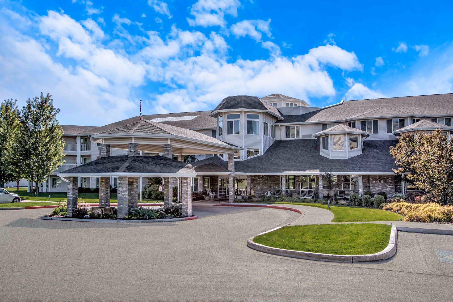 Front entrance of a multi-story senior living facility with a covered porte-cochere and circular driveway.