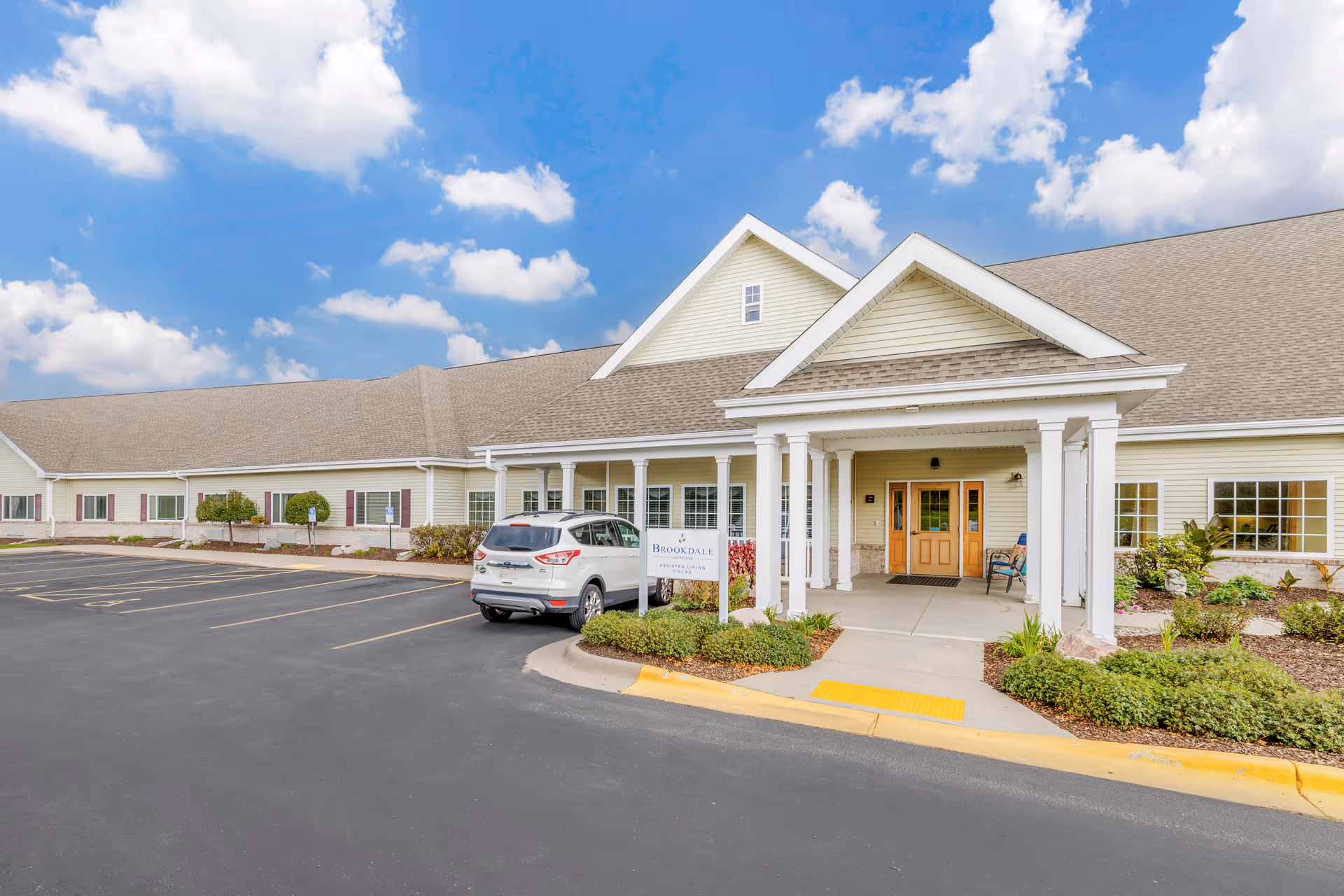 Exterior of a single-story senior living facility with beige siding and white-columned entrance.