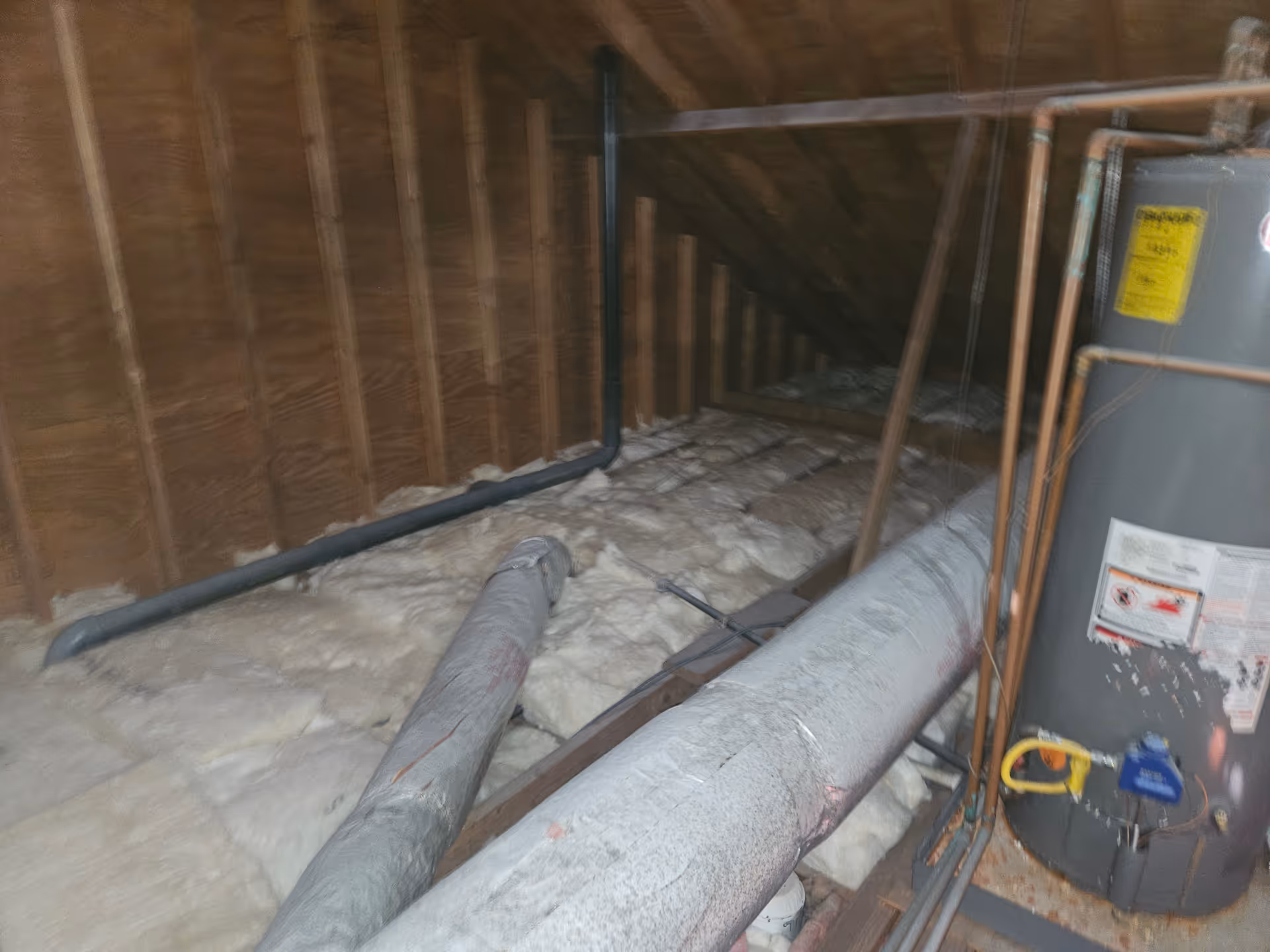 Attic utility space with exposed insulation, pipes, and a water heater.