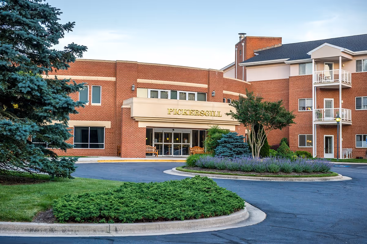 Exterior front view of Pickersgill Retirement Community building with a circular driveway, landscaped greenery, and trees in the foreground.
