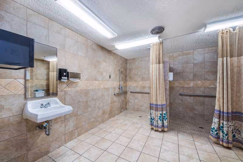 Public-style communal bathroom with tiled walls, sink, mirror, and two curtained showers.