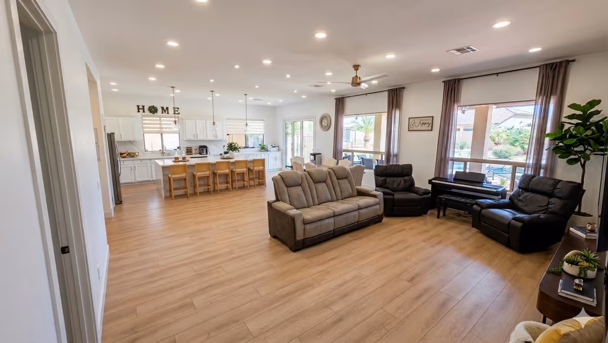 Spacious open-plan living area with sofa set, piano, and kitchen island at Coventry Royal Care LLC.