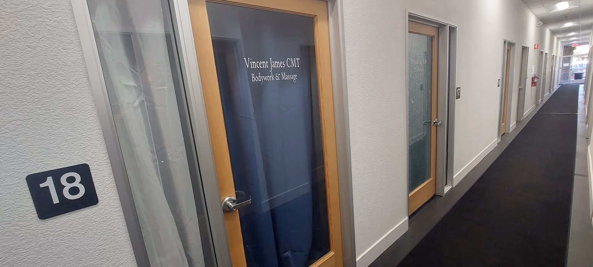 Interior hallway at a senior facility with doors and a blue-curtained treatment room.
