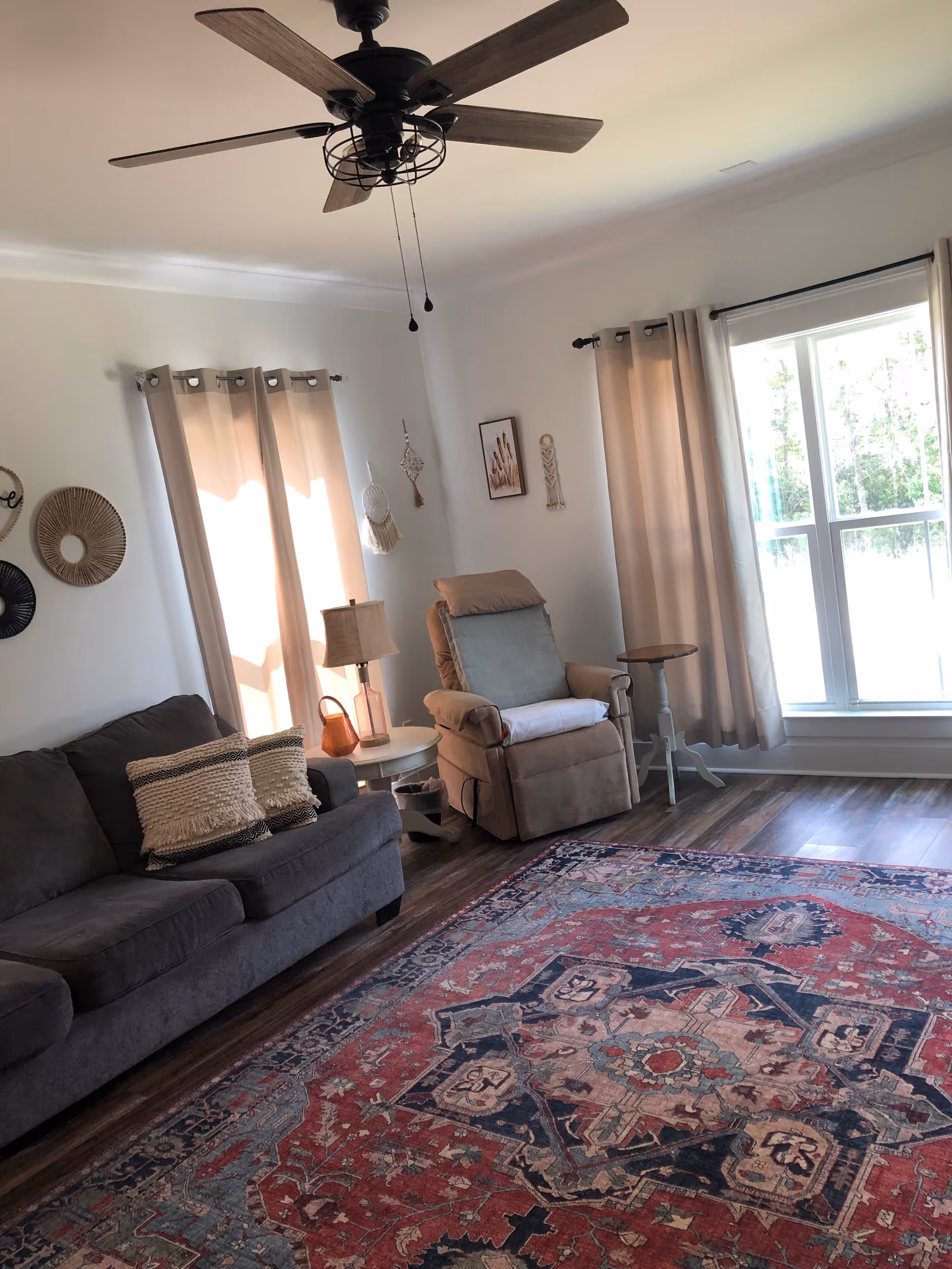 Cozy living room featuring a gray sofa, beige recliner, rug, and sunlit windows.