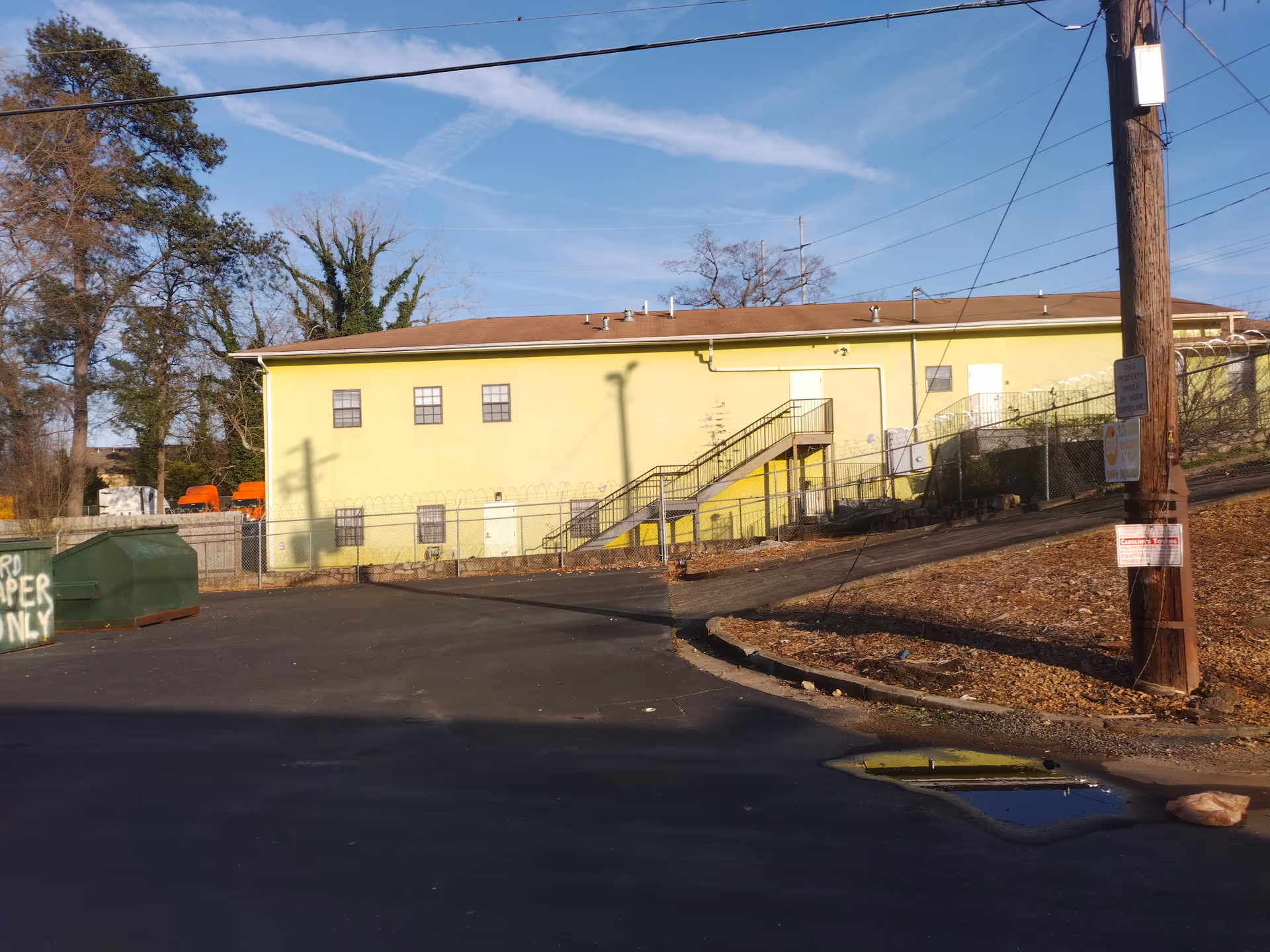 Exterior of a yellow building with stairs, fence, pole, and paved lot.