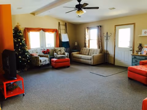 Cozy senior living common area with couches, chairs, a Christmas tree, and a ceiling fan.