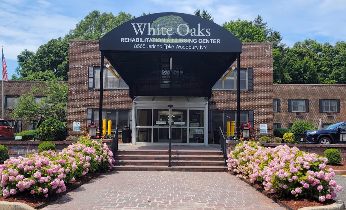 Brick building entrance with black awning, White Oaks Rehabilitation and Nursing Center, pink hydrangea bushes.