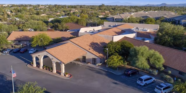 Aerial view of Mountain View Care Center's single-story building with terracotta tile roofs, a covered entrance, parking lot, and surrounding trees.