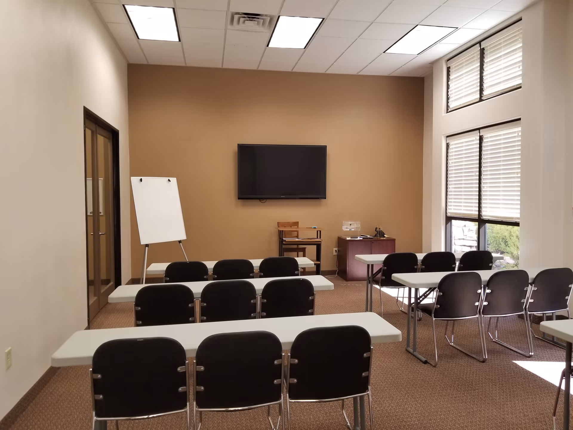 An interior conference room with whiteboards, tables, stacked chairs, and a wall-mounted TV.