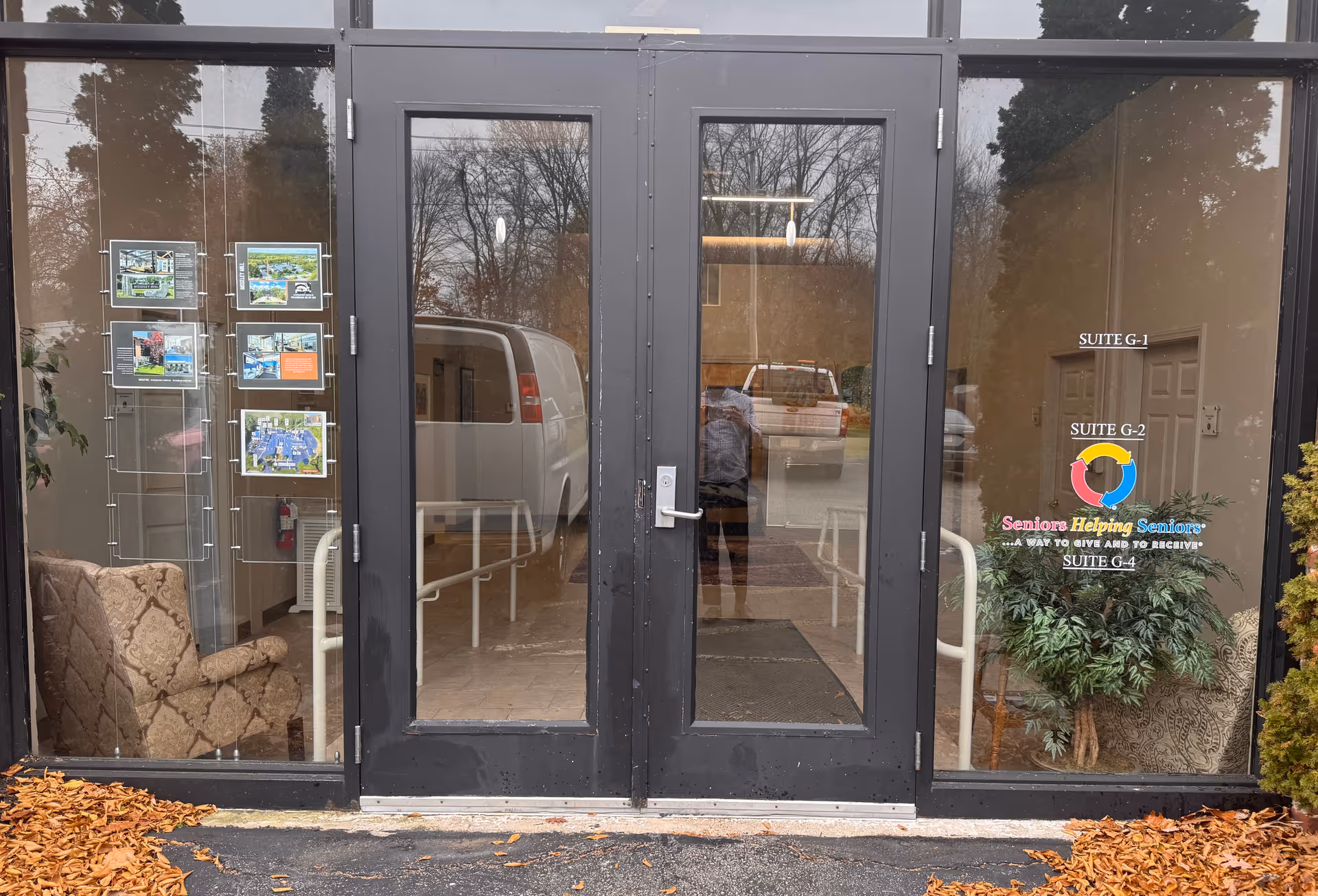 Glass entrance doors to a seniors facility with a lobby, brochure rack, and autumn leaves.