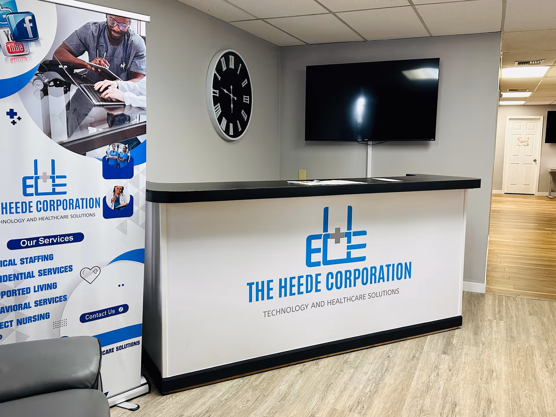 Reception desk in a lobby with a clock, TV, and Heede Corporation banner