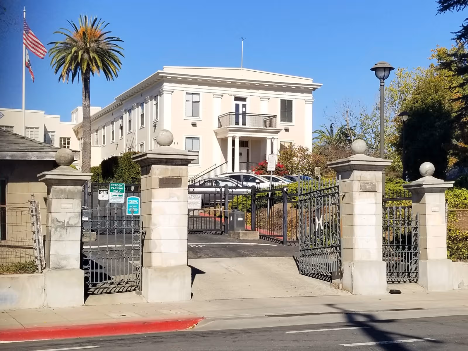 Gated entrance to Altenheim Senior Housing, a white multi-story building with palm trees and flags.