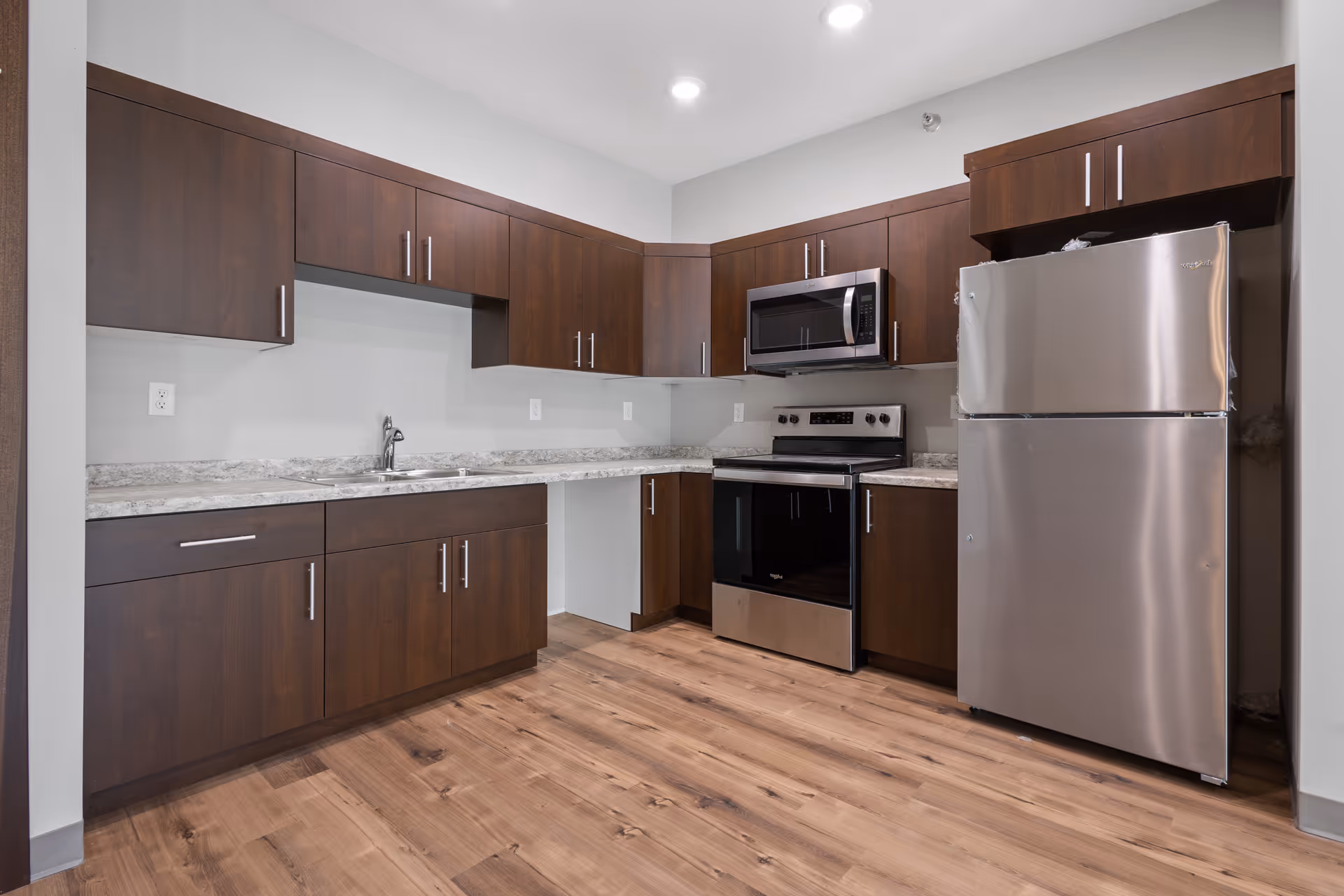 Modern kitchen with dark wood cabinets, stainless appliances, granite countertops, and wooden flooring.