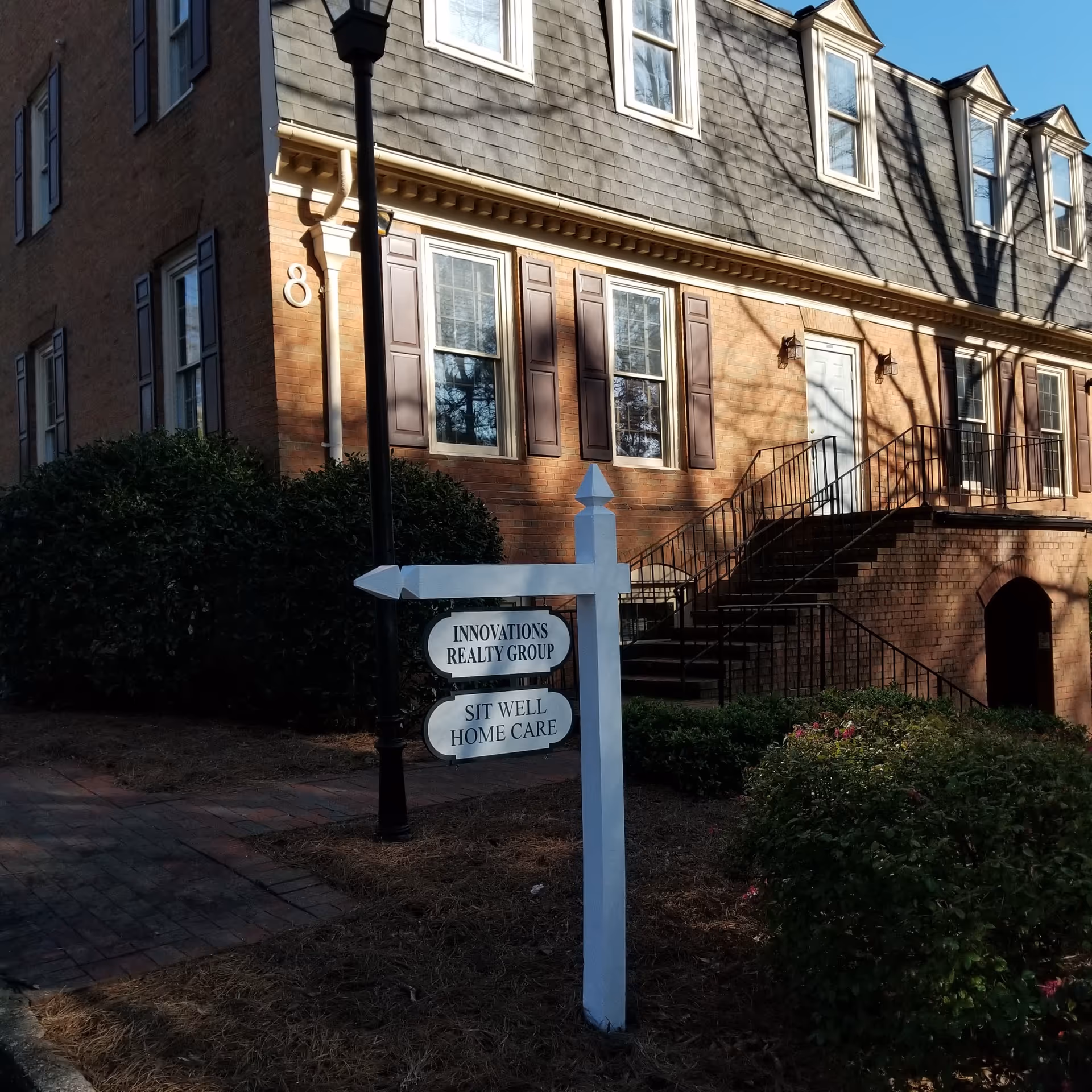 Brick senior living building with front stairs, windows, and a sign reading Sit Well Home Care.