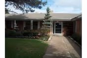 Brick single-story building entrance with walkway and manicured landscaping at front