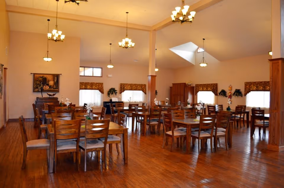 Spacious communal dining room with multiple wooden tables and chairs, warm lighting, and hardwood floors.