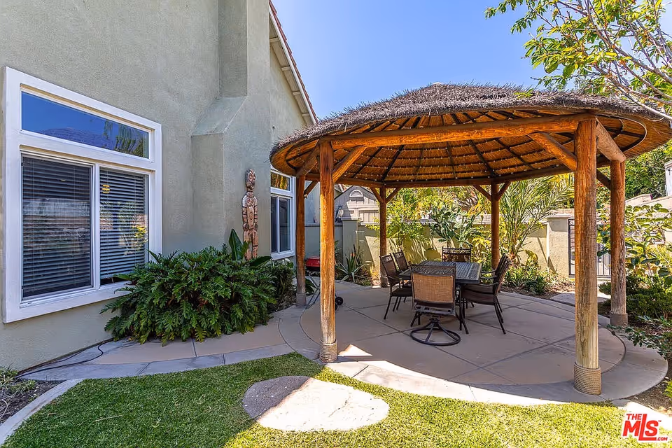 Outdoor patio with thatched gazebo and dining table beside a beige house