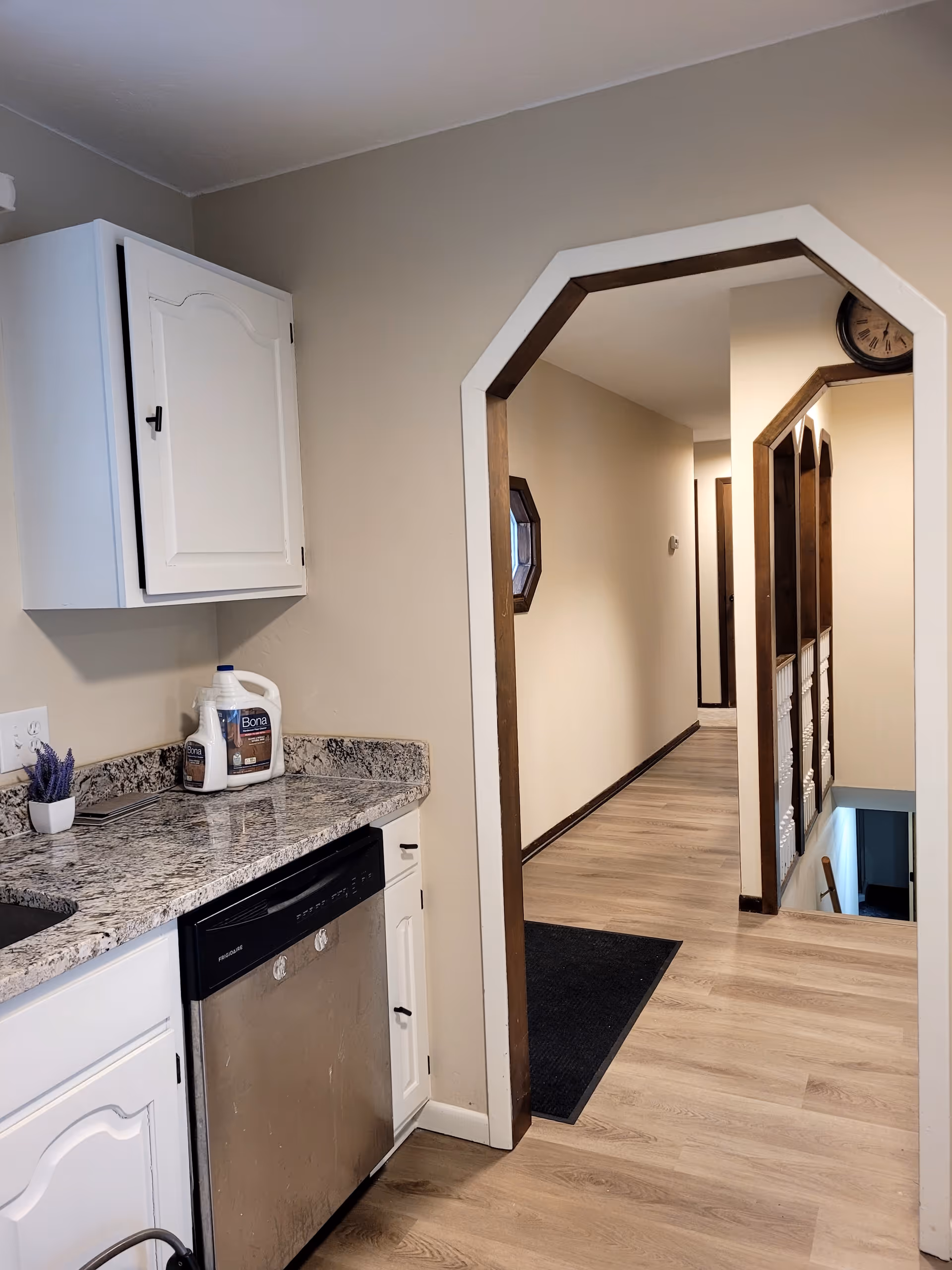Bright kitchen with granite countertops, white cabinets, and a stainless dishwasher, hallway beyond.