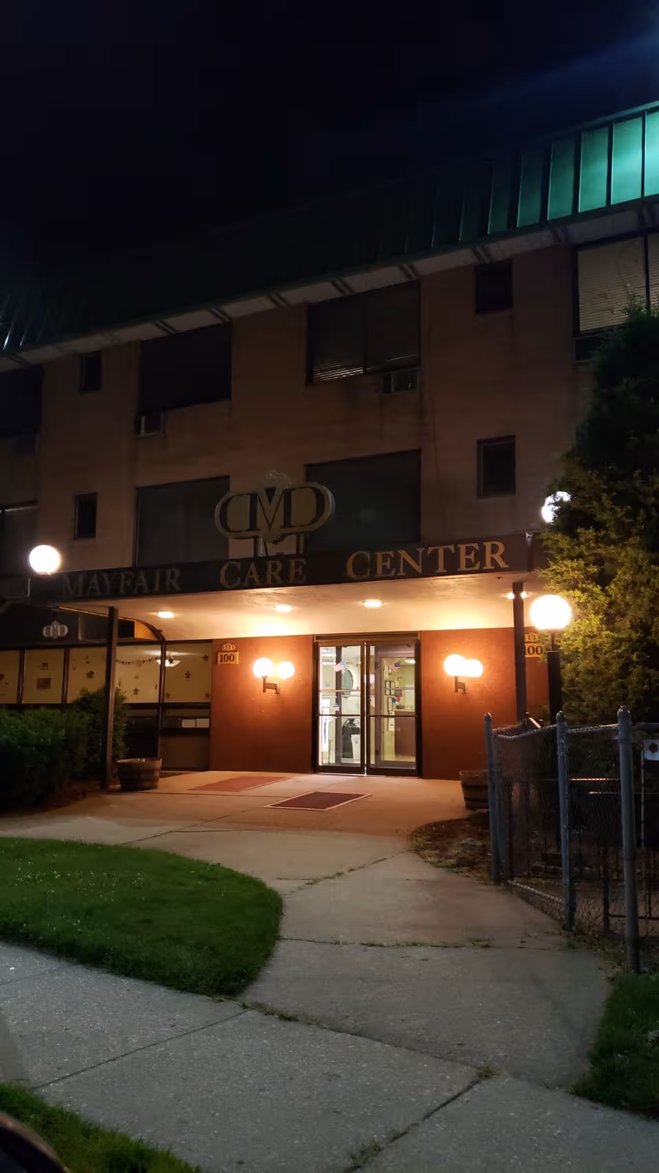 Night exterior of Mayfair Care Center with lit entrance and sign.