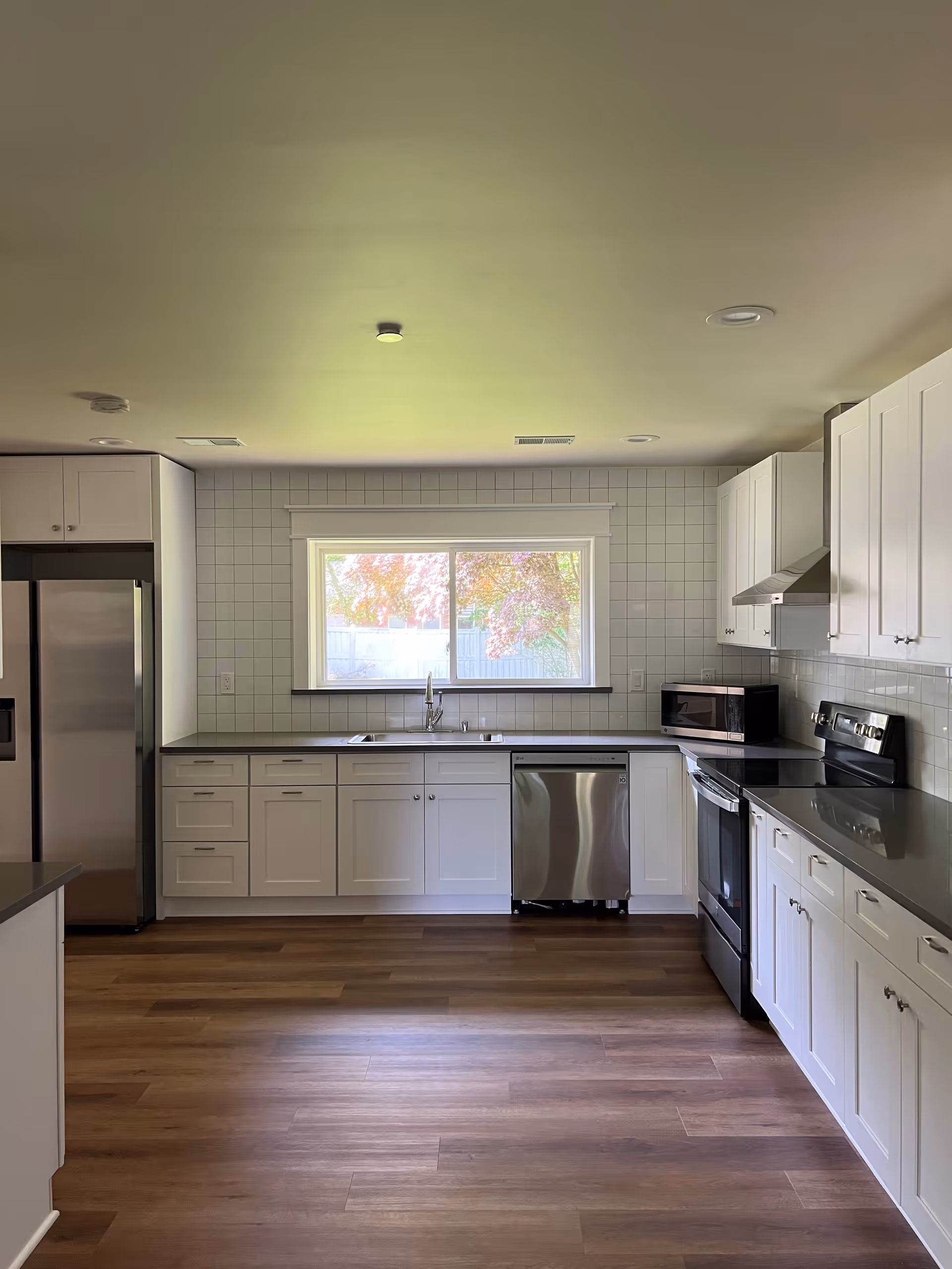Bright modern kitchen with white cabinets, stainless steel appliances, and a window.