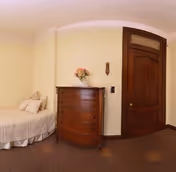 Small bedroom with a single bed, a wooden dresser topped with flowers, and a closed wooden door.