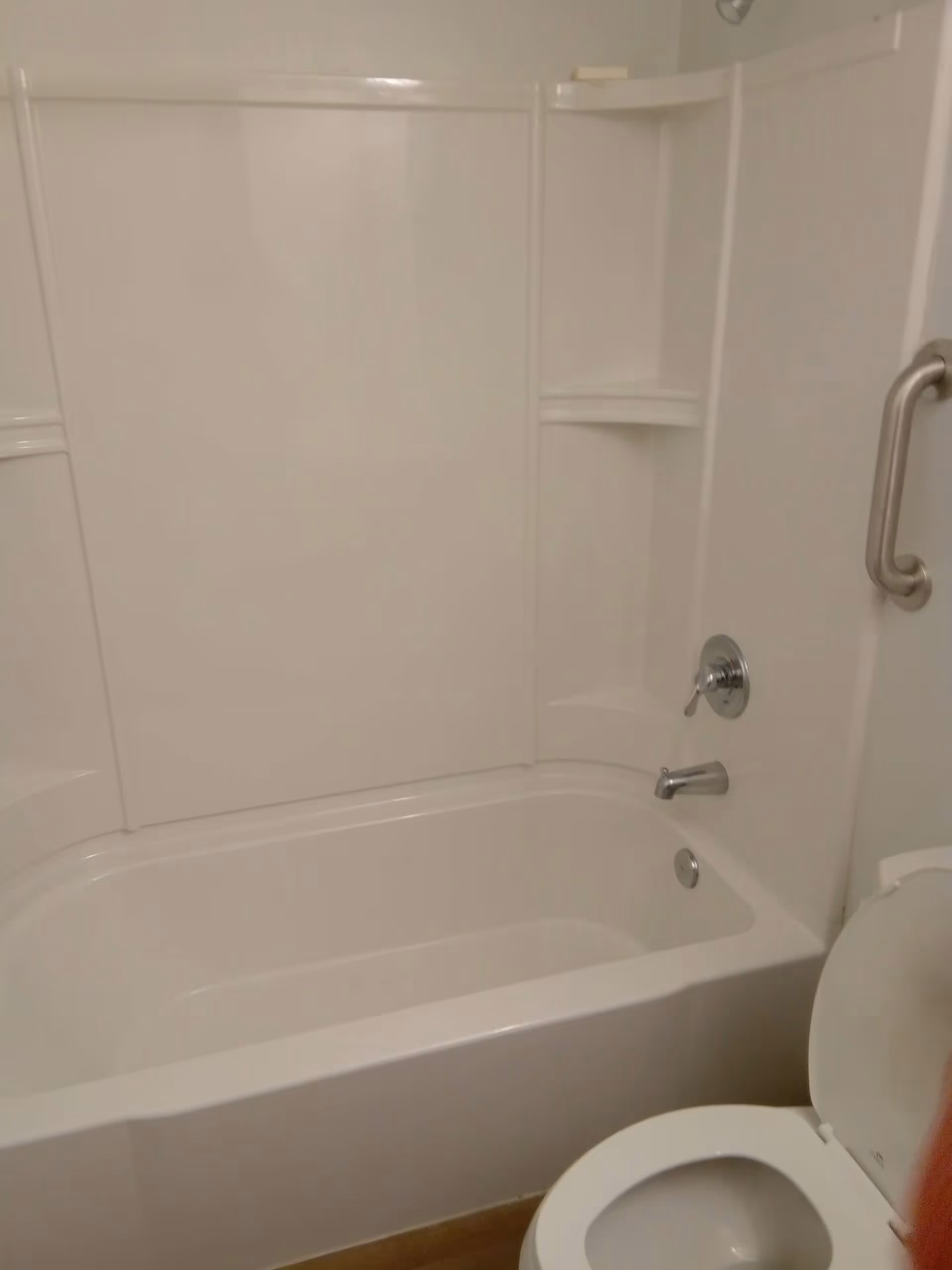 White bathtub with shower surround and grab bar in a compact residential bathroom.