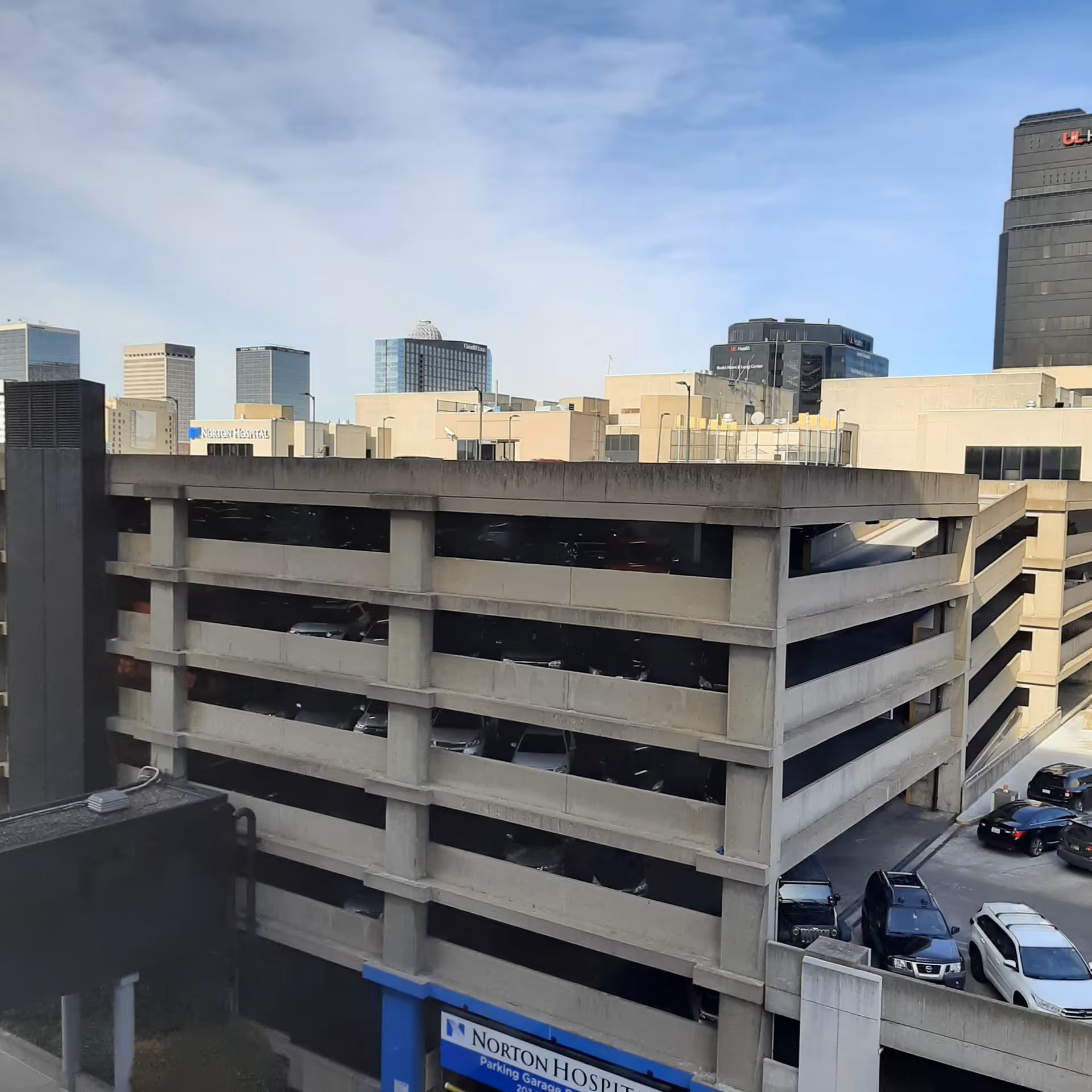 View of a downtown parking garage with surrounding high-rise buildings against a blue sky.