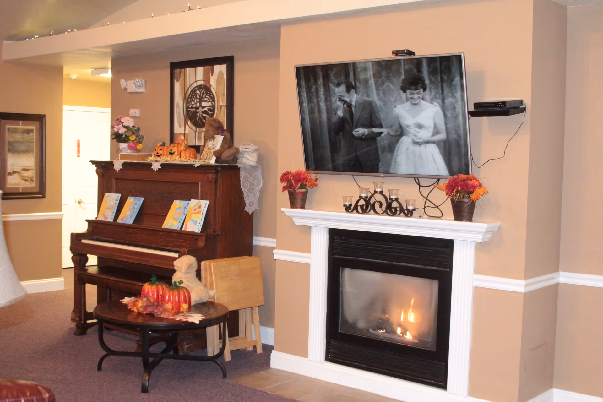 Cozy indoor living room with fireplace, mantel decorations, mounted TV, and a piano against the wall.