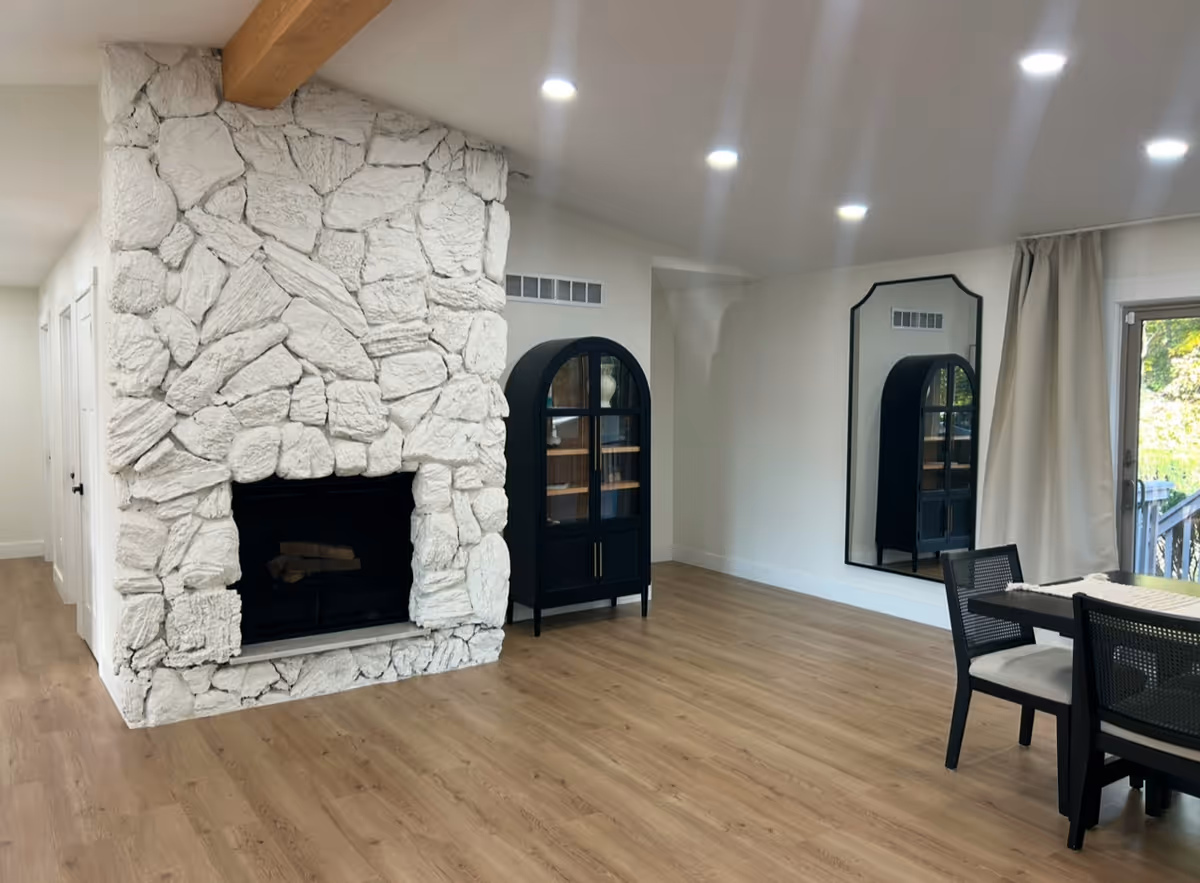 Bright living room with a white stone fireplace, wood floor, and dining area.
