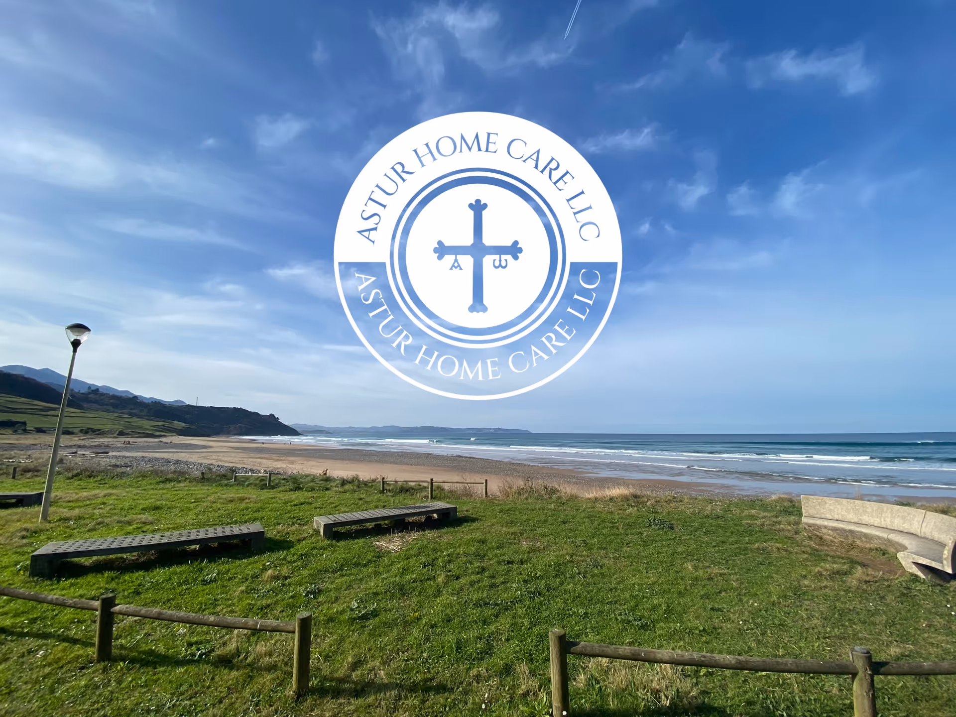 Beachside park with benches, grassy area, ocean shoreline, blue sky, and circular logo overlay.