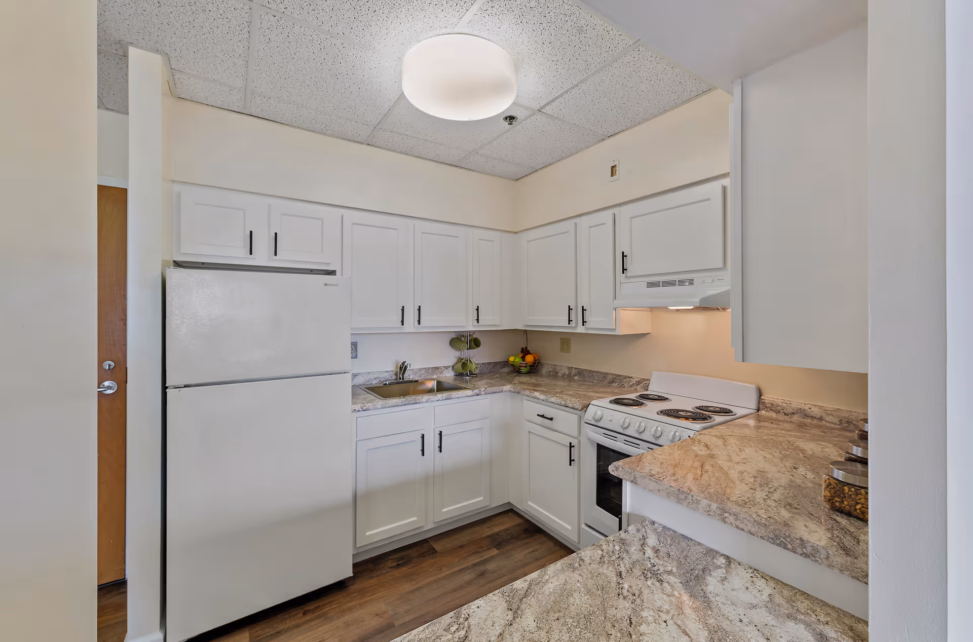 Bright white kitchen with cabinets, fridge, stove, sink, and marbled countertops.