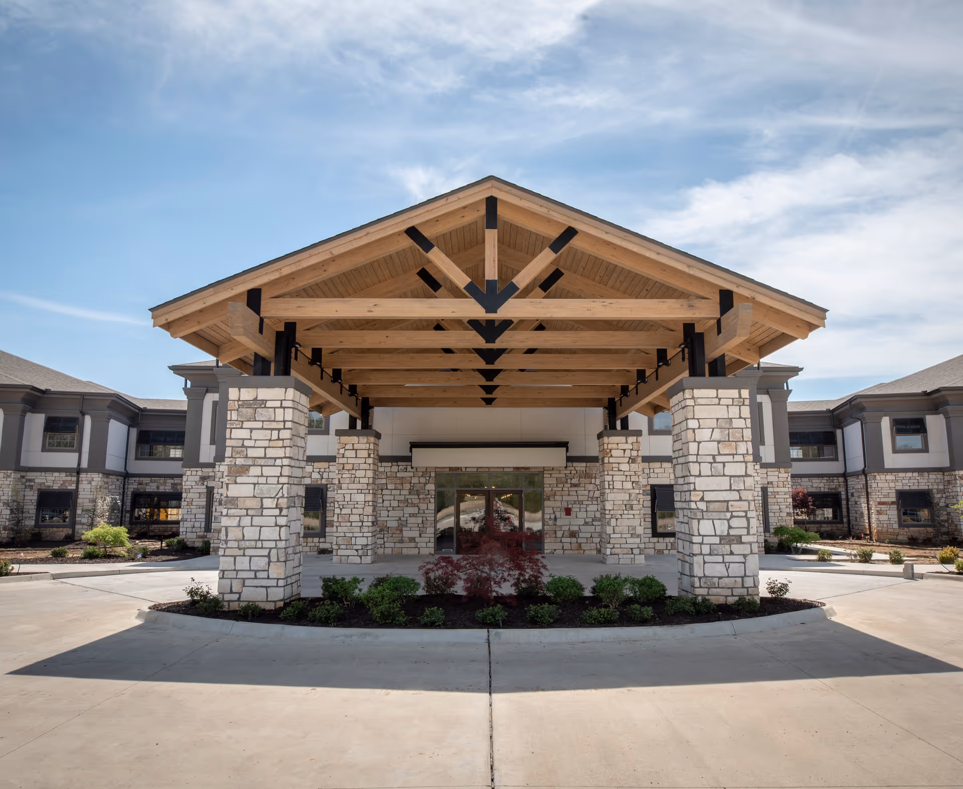 Stone entrance with wooden vaulted canopy supported by stone pillars at a senior facility.